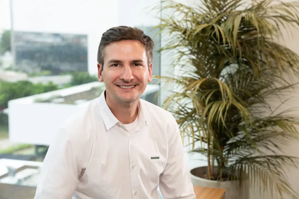 Stephano Galvão, Diretor de Operações da Norcoast, sorrindo e posando em ambiente corporativo com plantas ao fundo.
